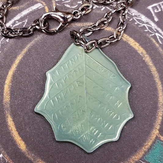 This Elvish Mithril Leaf of Spring Necklace is crafted in celebration of The Lord of the Rings by J. R. R. Tolkien. The leaf-shaped coin is struck from solid niobium, measures 2.7 cm in diameter, and weighs about 6.5 grams. Includes a 30" antique bronze cable chain with clasp. Coin artwork by Greg Franck-Weiby. Coins are struck one at a time in the USA using antique machinery and traditional coining techniques. A colorful description is included with history, translations, and facts about the coins.