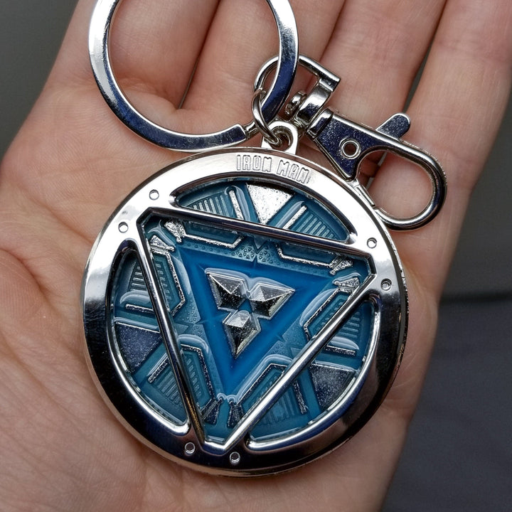 Iron Man Glow-In-The-Dark Pewter Arc Reactor Keychain.  In Celebration of Tony Stark’s Iron Man as seen in the Marvel Studios Avengers films, this oversize pewter Arc Reactor glow-in-the-dark metal keychain features the Arc Reactor powering Tony’s chest and power suit in Iron Man 3.  2 inches across &amp; nearly 1/2 inch thick!  Features “Iron Man” logo on the back Includes stainless steel keyring and clip Blue Glow-in-the-Dark effect!  Carry your own Proof that Tony Stark Has a Heart