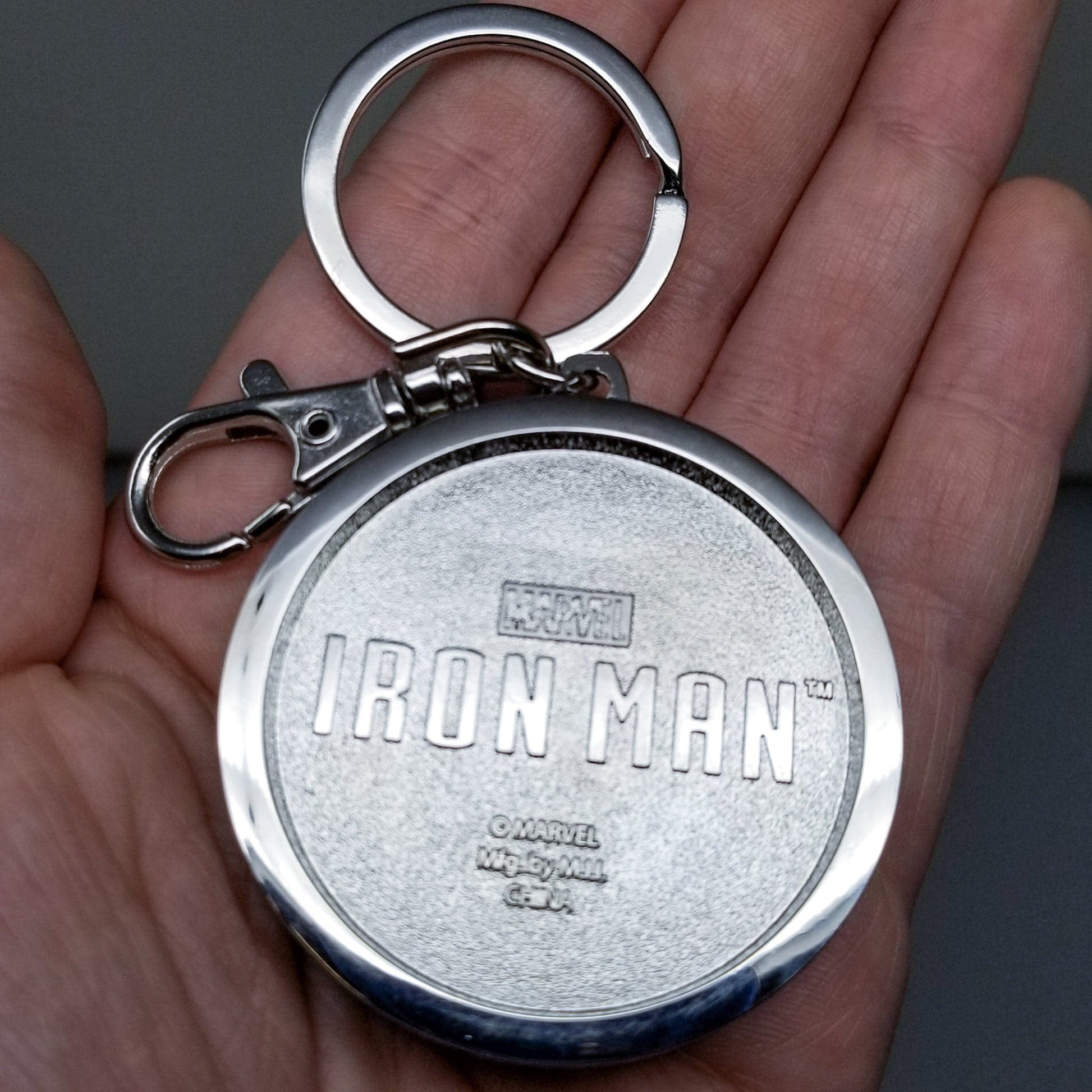 Iron Man Glow-In-The-Dark Pewter Arc Reactor Keychain.  In Celebration of Tony Stark’s Iron Man as seen in the Marvel Studios Avengers films, this oversize pewter Arc Reactor glow-in-the-dark metal keychain features the Arc Reactor powering Tony’s chest and power suit in Iron Man 3.  2 inches across & nearly 1/2 inch thick!  Features “Iron Man” logo on the back Includes stainless steel keyring and clip Blue Glow-in-the-Dark effect!  Carry your own Proof that Tony Stark Has a Heart