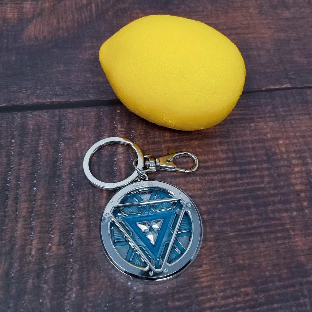 Iron Man Glow-In-The-Dark Pewter Arc Reactor Keychain.  In Celebration of Tony Stark’s Iron Man as seen in the Marvel Studios Avengers films, this oversize pewter Arc Reactor glow-in-the-dark metal keychain features the Arc Reactor powering Tony’s chest and power suit in Iron Man 3.  2 inches across &amp; nearly 1/2 inch thick!  Features “Iron Man” logo on the back Includes stainless steel keyring and clip Blue Glow-in-the-Dark effect!  Carry your own Proof that Tony Stark Has a Heart