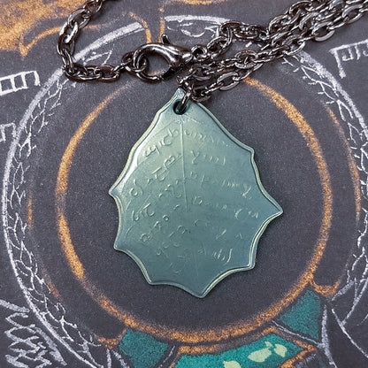 This Elvish Mithril Leaf of Spring Necklace is crafted in celebration of The Lord of the Rings by J. R. R. Tolkien. The leaf-shaped coin is struck from solid niobium, measures 2.7 cm in diameter, and weighs about 6.5 grams. Includes a 30" antique bronze cable chain with clasp. Coin artwork by Greg Franck-Weiby.  Coins are struck one at a time in the USA using antique machinery and traditional coining techniques. A colorful description is included with history, translations, and facts about the coins.