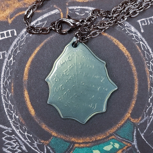 This Elvish Mithril Leaf of Spring Necklace is crafted in celebration of The Lord of the Rings by J. R. R. Tolkien. The leaf-shaped coin is struck from solid niobium, measures 2.7 cm in diameter, and weighs about 6.5 grams. Includes a 30" antique bronze cable chain with clasp. Coin artwork by Greg Franck-Weiby.  Coins are struck one at a time in the USA using antique machinery and traditional coining techniques. A colorful description is included with history, translations, and facts about the coins.