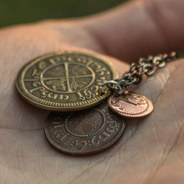 A layered necklace containing a set of three coins from the Shire in the The Lord of the Rings.  A 30" chain holds three coins from The Shire coins: a brass Shire Tuppence, a copper Shire Penny, and a tiny copper Shire Farthing. Coin text is inscribed in Tengwar. The coins will each feature a tree that will be one of the following variants: pine, elm, willow, and oak. The card inside provides translation of the coin text on each coin. 