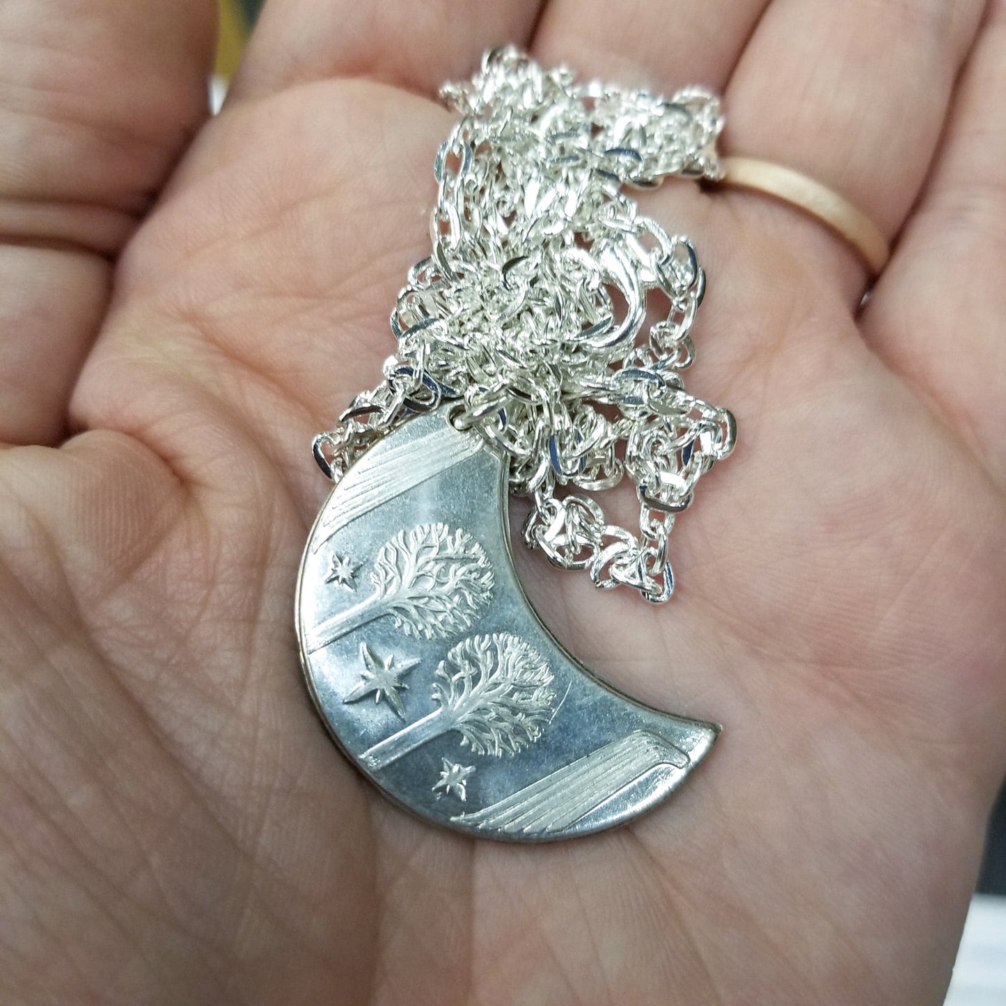 Elvish coin from Rivendell is shaped like a crescent moon. It depicts the valley containing the ancient trees of silver and gold and the three Silmarils, represented as stars. The text in Tengwar translates from Sindarin to Elrond Peredhil, Lord of Rivendell, The Last Homely House East of the Sea. It includes the date that Thorin and Company meet Elrond at Rivendell before continuing on to The Lonely Mountain.  This Rivendell Moon is crafted in celebration of The Lord of the Rings by J. R. R. Tolkien