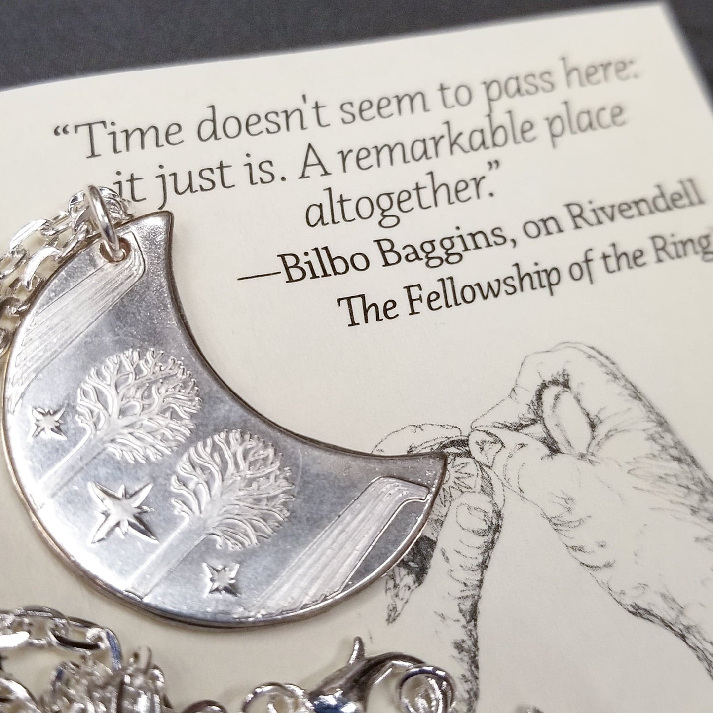 Elvish coin from Rivendell is shaped like a crescent moon. It depicts the valley containing the ancient trees of silver and gold and the three Silmarils, represented as stars. The text in Tengwar translates from Sindarin to Elrond Peredhil, Lord of Rivendell, The Last Homely House East of the Sea. It includes the date that Thorin and Company meet Elrond at Rivendell before continuing on to The Lonely Mountain.  This Rivendell Moon is crafted in celebration of The Lord of the Rings by J. R. R. Tolkien