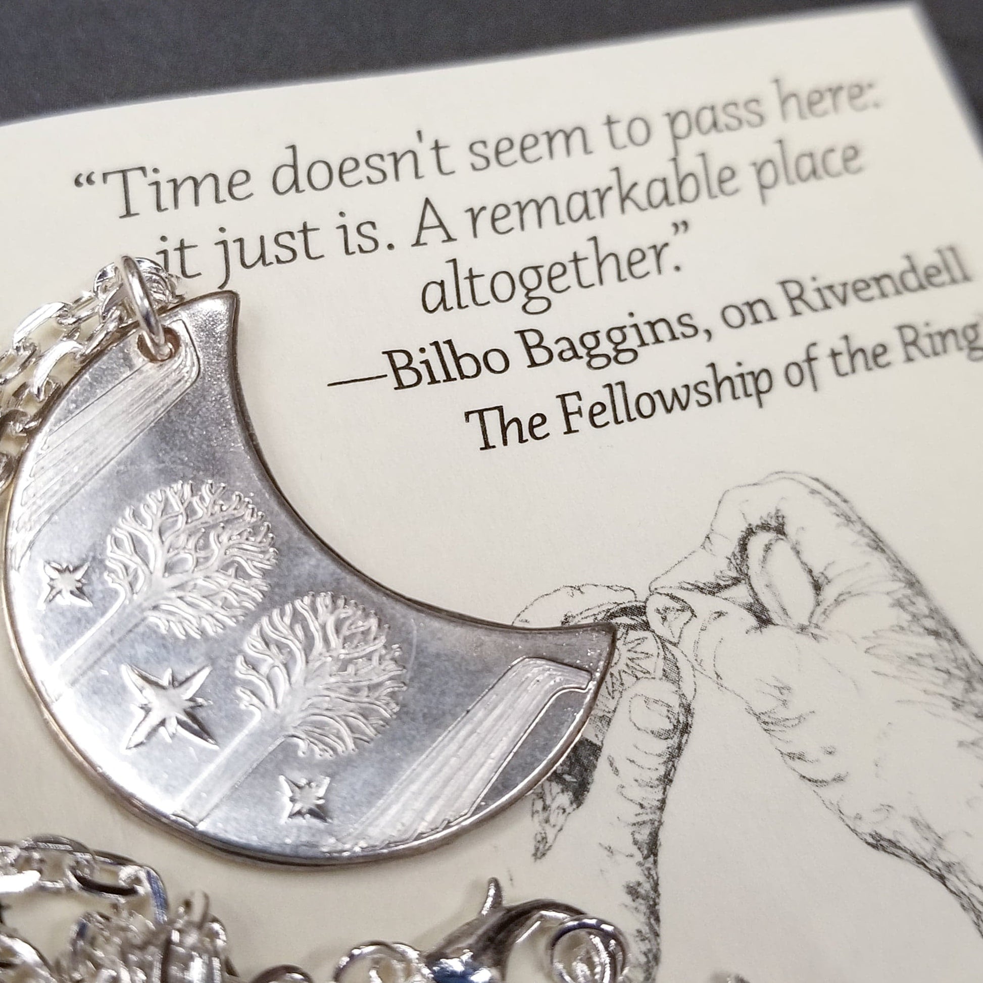 Elvish coin from Rivendell is shaped like a crescent moon. It depicts the valley containing the ancient trees of silver and gold and the three Silmarils, represented as stars. The text in Tengwar translates from Sindarin to Elrond Peredhil, Lord of Rivendell, The Last Homely House East of the Sea. It includes the date that Thorin and Company meet Elrond at Rivendell before continuing on to The Lonely Mountain.  This Rivendell Moon is crafted in celebration of The Lord of the Rings by J. R. R. Tolkien