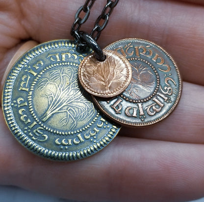 A layered necklace containing a set of three coins from the Shire in the The Lord of the Rings.  A 30" chain holds three coins from The Shire coins: a brass Shire Tuppence, a copper Shire Penny, and a tiny copper Shire Farthing. Coin text is inscribed in Tengwar. The coins will each feature a tree that will be one of the following variants: pine, elm, willow, and oak. The card inside provides translation of the coin text on each coin. 