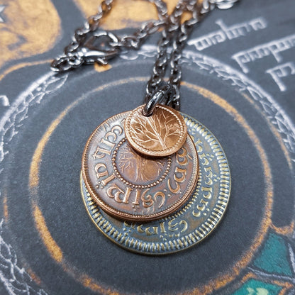 A layered necklace containing a set of three coins from the Shire in the The Lord of the Rings.  A 30" chain holds three coins from The Shire coins: a brass Shire Tuppence, a copper Shire Penny, and a tiny copper Shire Farthing. Coin text is inscribed in Tengwar. The coins will each feature a tree that will be one of the following variants: pine, elm, willow, and oak. The card inside provides translation of the coin text on each coin. 