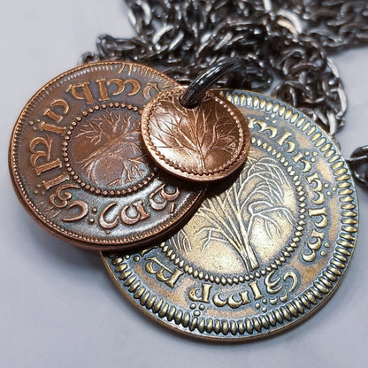 A layered necklace containing a set of three coins from the Shire in the The Lord of the Rings.  A 30" chain holds three coins from The Shire coins: a brass Shire Tuppence, a copper Shire Penny, and a tiny copper Shire Farthing. Coin text is inscribed in Tengwar. The coins will each feature a tree that will be one of the following variants: pine, elm, willow, and oak. The card inside provides translation of the coin text on each coin. 