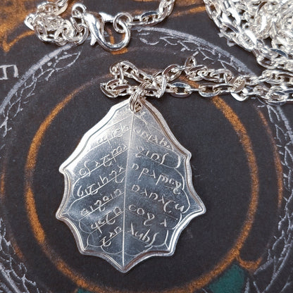 This Elvish Mithril Leaf of Spring Necklace is crafted in celebration of The Lord of the Rings by J. R. R. Tolkien. The leaf-shaped coin is struck from solid silver, measures 2.7 cm in diameter, and weighs about 6.5 grams. Includes a 30" antique bronze cable chain with clasp. Coin artwork by Greg Franck-Weiby.  Coins are struck one at a time in the USA using antique machinery and traditional coining techniques. A colorful description is included with history, translations, and facts about the coins.